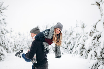 The guy holds the girl in his arms in the snowy winter forest