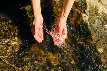The girl traveler washes her hands in cold river water. Sun glare on clear natural mountain water....