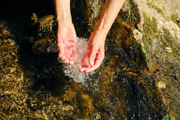 The girl traveler washes her hands in cold river water. Sun glare on clear natural mountain water....