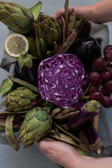 Tray covered by a rustic napkin full of purple and green vegetables held by woman hands.