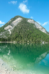 Fototapeta premium A panoramic view on the Pragser Wildsee, a lake in South Tyrolean Dolomites. High mountain chains around the lake. The sky and mountains are reflecting in the lake. Dense forest at the shore. Serenity