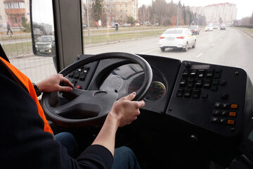 The hands of a young and confident driver lying on the wheel of a bus traveling along the road.