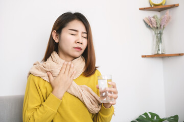 sick Asian woman suffering from sore throat hand holding glass of hot water