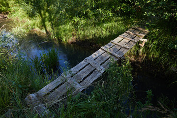 Fototapeta premium A homemade bridge made of gray old boards across the river in a Russian village in summer on a sunny day