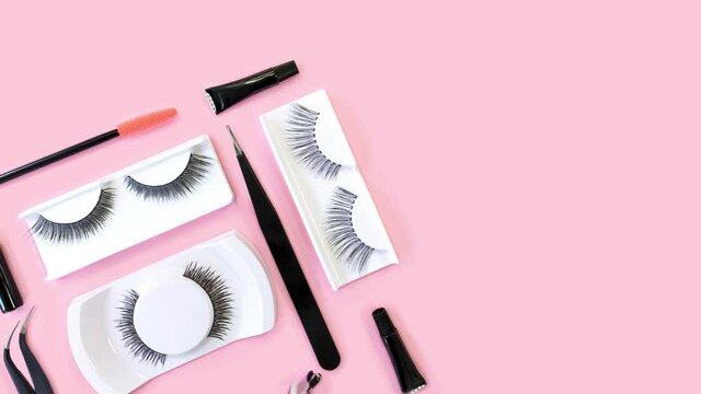 Fake eyelashes. Tools for eye lash extensions on trendy pastel pink background. Knolling concept. Eyelash curler, tweezers, brushes. Makeup accessories. Cosmetic products. Stop motion animation.