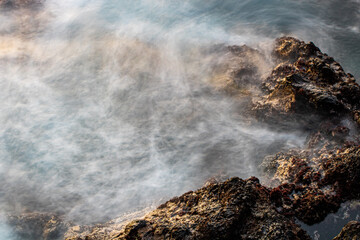Sunset seascape with sea water in motion blur, stones on the beach. Atlantic ocean, Tenerife island. Long exposure. Background