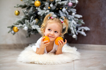 Little girl holds tangerines in her hands against the background of the Christmas tree.