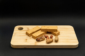 A shot of peeled peanuts, peanuts in the shell, and peanut nougat bars on a cutting board, in the...
