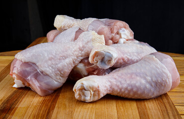A bunch of raw chicken legs lie on a wooden board.