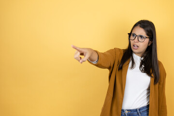 Young beautiful woman wearing a blazer over isolated yellow background pointing with finger...