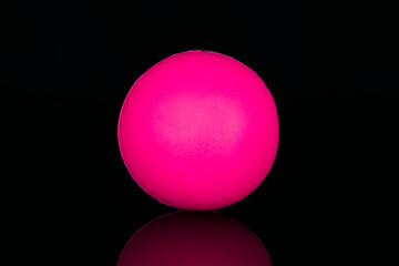 Antistress pink happy face icon ball on black reflective surface.