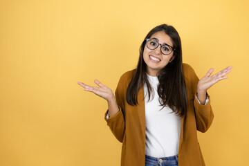 Young beautiful woman wearing a blazer over isolated yellow background clueless and confused...