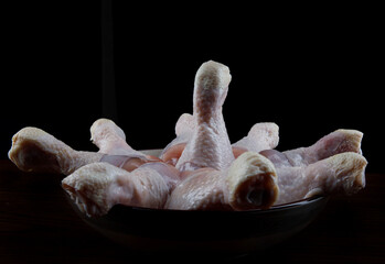 Raw chicken legs are folded in a plate. Chicken on a dark background.