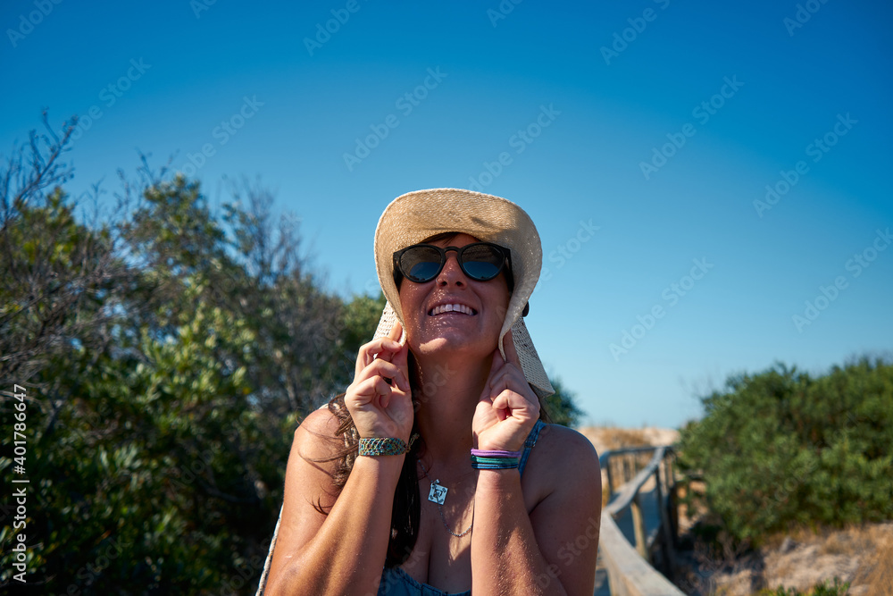 Wall mural a cheerful female in a cute panama hat and sunglasses enjoying summertime ou