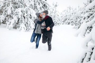 Fototapeta na wymiar Loving couple runs through a snowy forest in winter in a sweater and a scarf and smiles