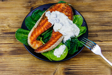 Grilled salmon steak with spinach and tartare sauce on wooden table. Top view
