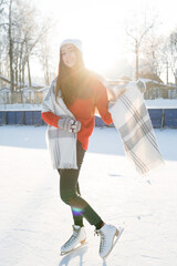 A girl with long hair stands on skates in a hat and mittens on a sunny frosty day