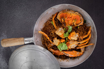 Baked fresh sea crab with vermicelli or glass noodle in the cook pot with table set up ready to eat. Black background
