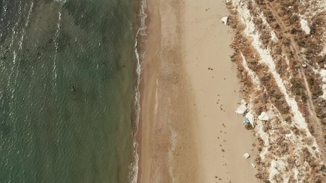 
Aerial view of the beach in the Mediterranean Sea with a rocky shore. The drone flies parallel to the ground where you can see how the waves crash against the yellow sand and rocks.