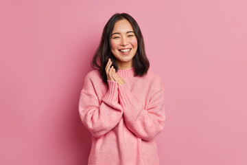 Portrait of sincere brunette Asian female model rubs palms and smiles broadly expresses happiness...
