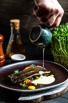 Chef hands cooking fish dish roasted trout, vegetables and white creamy sauce in a freeze motion. vertical image, place for text