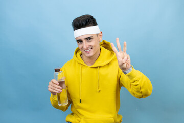 Young caucasian man wearing sportswear holding water bottle over isolated blue background showing and pointing up with fingers number three while smiling confident and happy