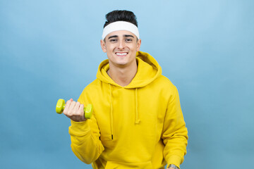 Young caucasian man wearing sportswear holding water bottle over isolated blue background smiling and holding a dumbbells