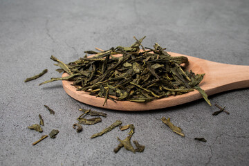 Spoon of dried green tea leaves on gray cement background