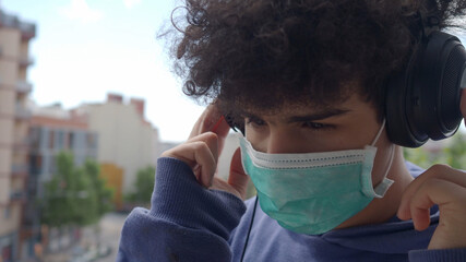 Afro teenage boy with a mask listening to music with headphones. Concept: security measures and...