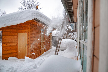 Real Russian winter, when frost and a lot of snow, in the country village, with small houses, dumping snow from the roof of a house