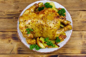 Baked whole chicken with potato on a wooden table. Top view