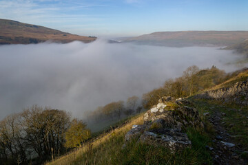 Above the clouds in the yorkshire hills. With a stone wall in the foreground.