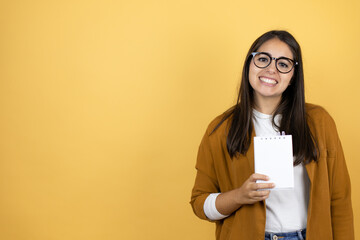 Young beautiful woman wearing a blazer over isolated yellow background smiling and showing blank notebook