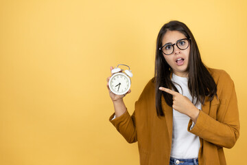 Young beautiful woman wearing a blazer over isolated yellow background pointing a clock with serious expression
