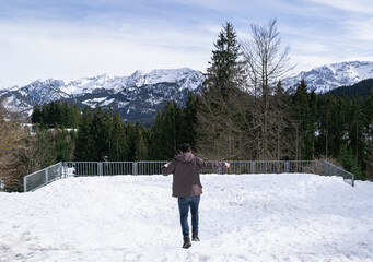 Happy young man springs in the snow in winter with the alps in the background, Allgäu, Germany