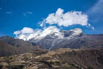 campo cultivado y cordillera de los majestuosos Andes imponentes y nevados con cielos azul intenso con nubes en Perú