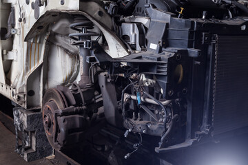 Obraz premium The front part of the car after an accident in a car repair service with a disassembled hood and metal grille and various parts in the garage box.