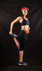 Beautiful girl in a jogging red uniform warming up before training in the studio on a black background