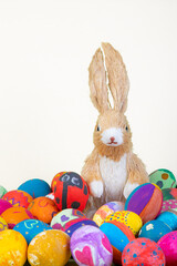 rabbit figurine between painted easter eggs before white background