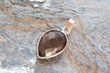 Sterling silver pendant with mineral faceted smokey quartz gemstone on rocky background