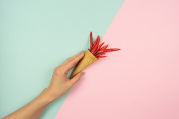 A woman’s hand holds a waffle cone with red hot peppers in it