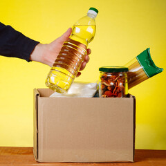 Donation box with food and hands of a volunteer. Macaroni, buckwheat, canned food, oil filling in a box. Volunteer assistance to the homeless and needy. Social support for people. square image