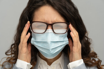 Business woman with foggy glasses from breath caused by wearing disposable mask on studio grey...