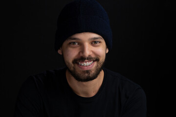 Closeup frontal portrait of young men over black background. He has a big smile and is wearing a...