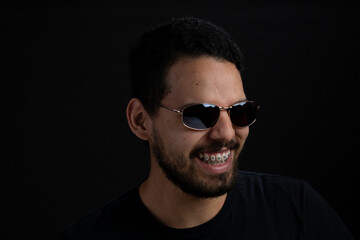 Obraz premium Closeup portrait of young men over black background. He is smiling to one side and is wearing sunglasses.