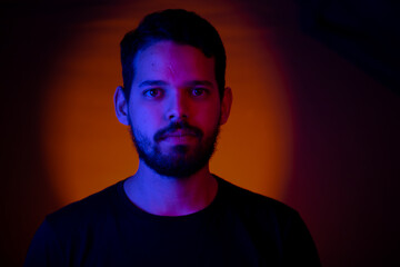Fototapeta premium Young man portrait with colored lights in a studio shot with an orange light in the background.