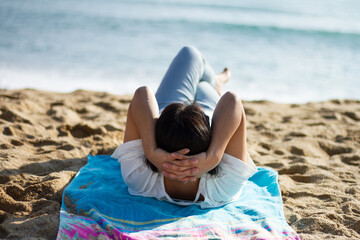 A Hispanic woman lying down on a towel on a sandy beach in Barcelona, Spain during daylight