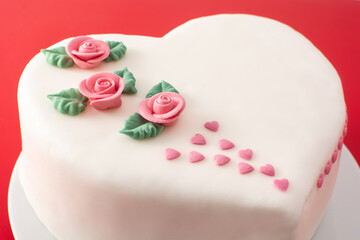Heart cake for St. Valentine's Day, Mother's Day, or Birthday, decorated with roses and pink sugar hearts on red background	