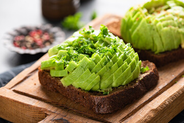 Vegan avocado and rye bread toast on wooden cutting board, closeup view