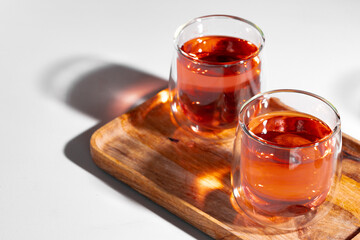 Two glass cups of fruit tea on wooden tray on white table
